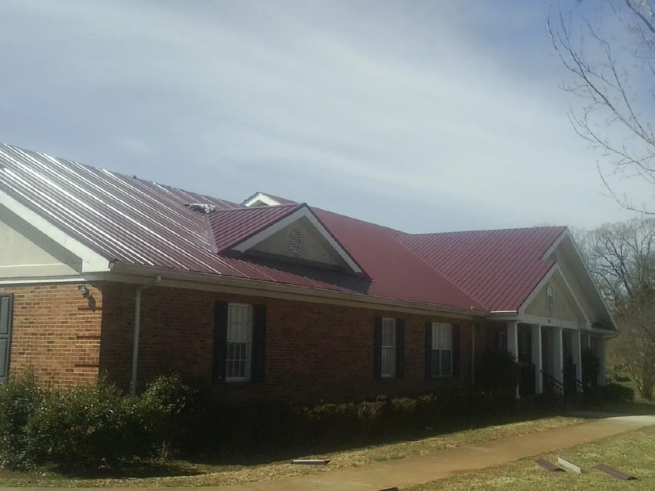 Red metal roof with gabled entries on a long brick building, from a Hail Damage Roof Repair job in Cowlesville