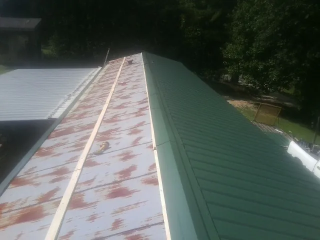 Old rusted panels beside newly installed green metal roofing — Wind Damage Roof Repair by Roofing Brothers in Cowlesville