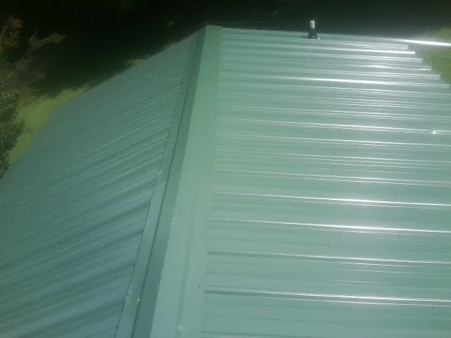 New green metal panels meeting at the ridge of a roof — Flat Roof Repair work by our crew in Cowlesville