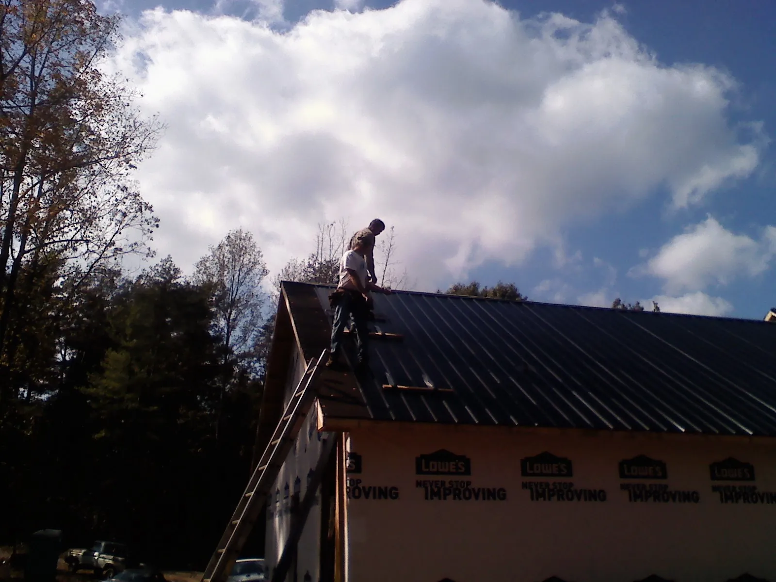 Roofer fastening dark metal panels high against a cloudy sky, from a Roof Inspection job in Cowlesville
