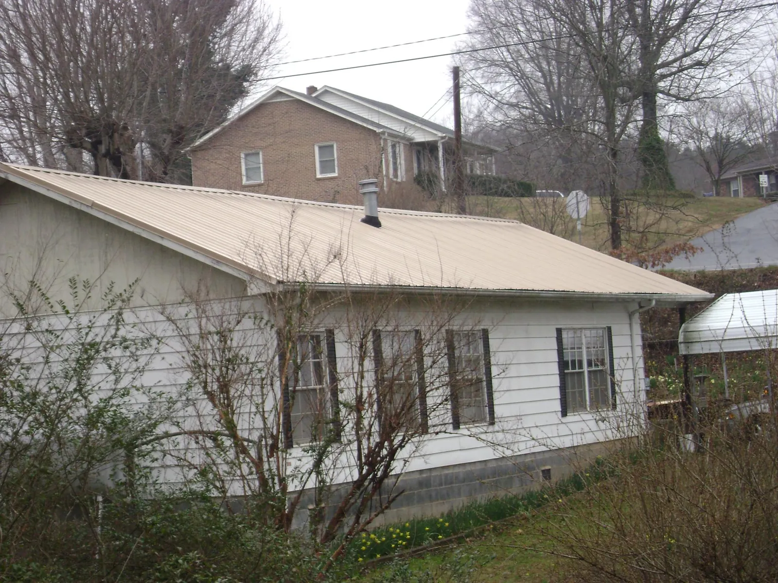 Tan metal roof on a white sided house set into a hillside — Commercial Roofing by Roofing Brothers in Cowlesville