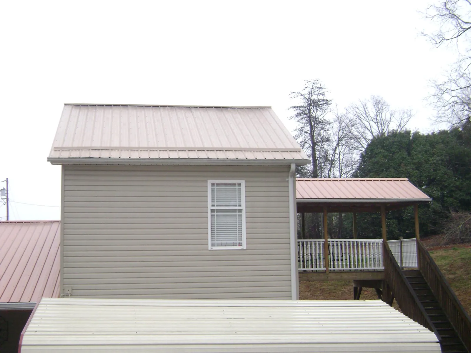 Tan metal roofs on a two story addition and attached porch, from a Roof Replacement job in Cowlesville